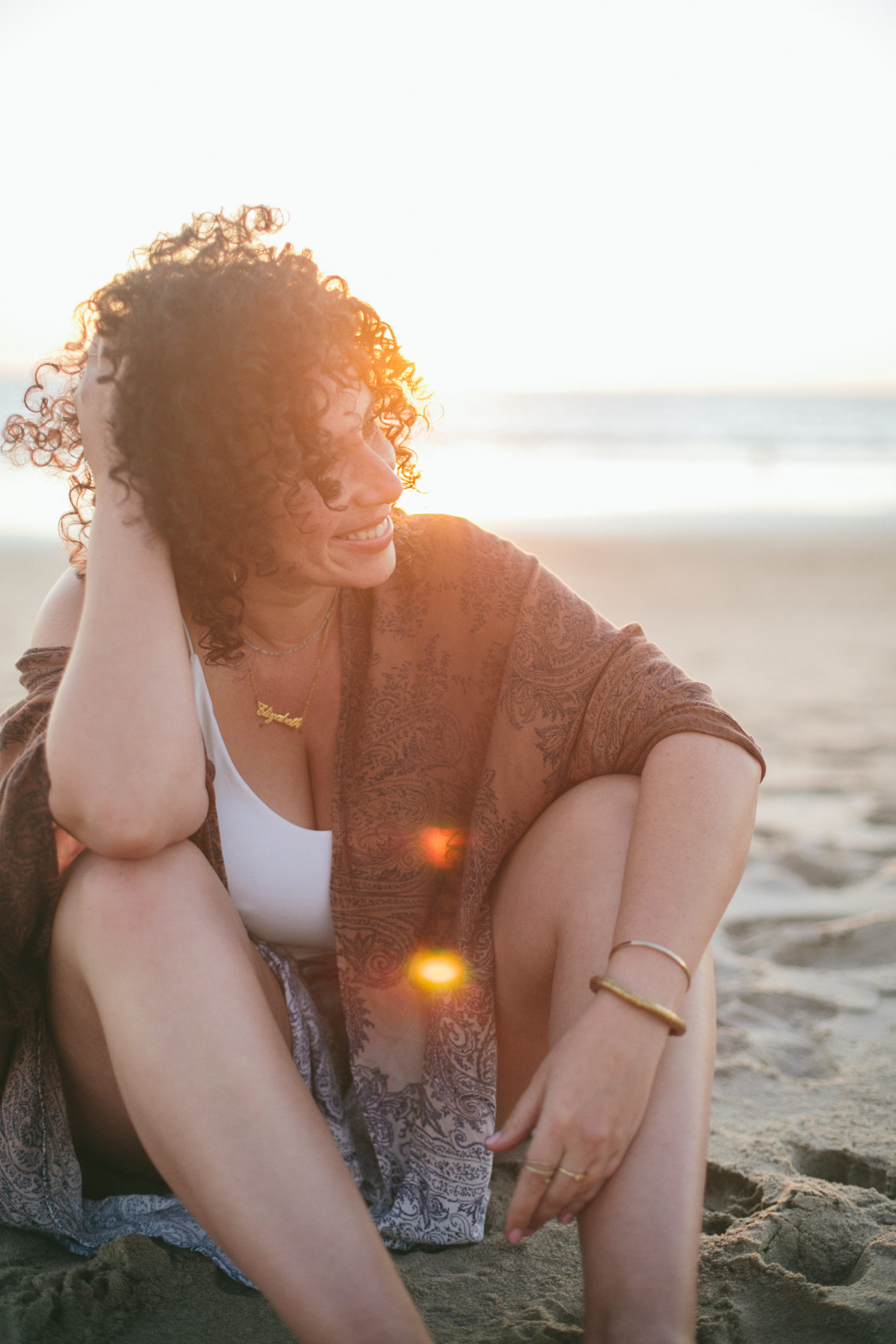 Elizabeth sitting on a beach at sunset smiling